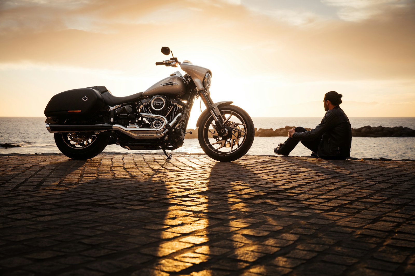 man sitting on ground beside parked silver cruiser motorcycle, motorcycle